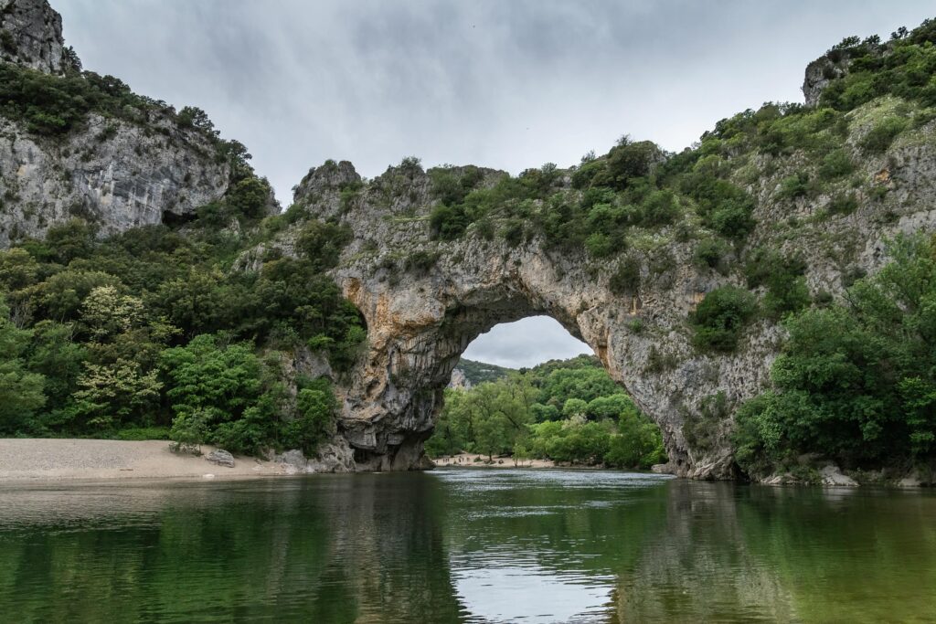 Scenic view of the natural arch at Vallon-Pont-d'Arc, France, over a tranquil river.