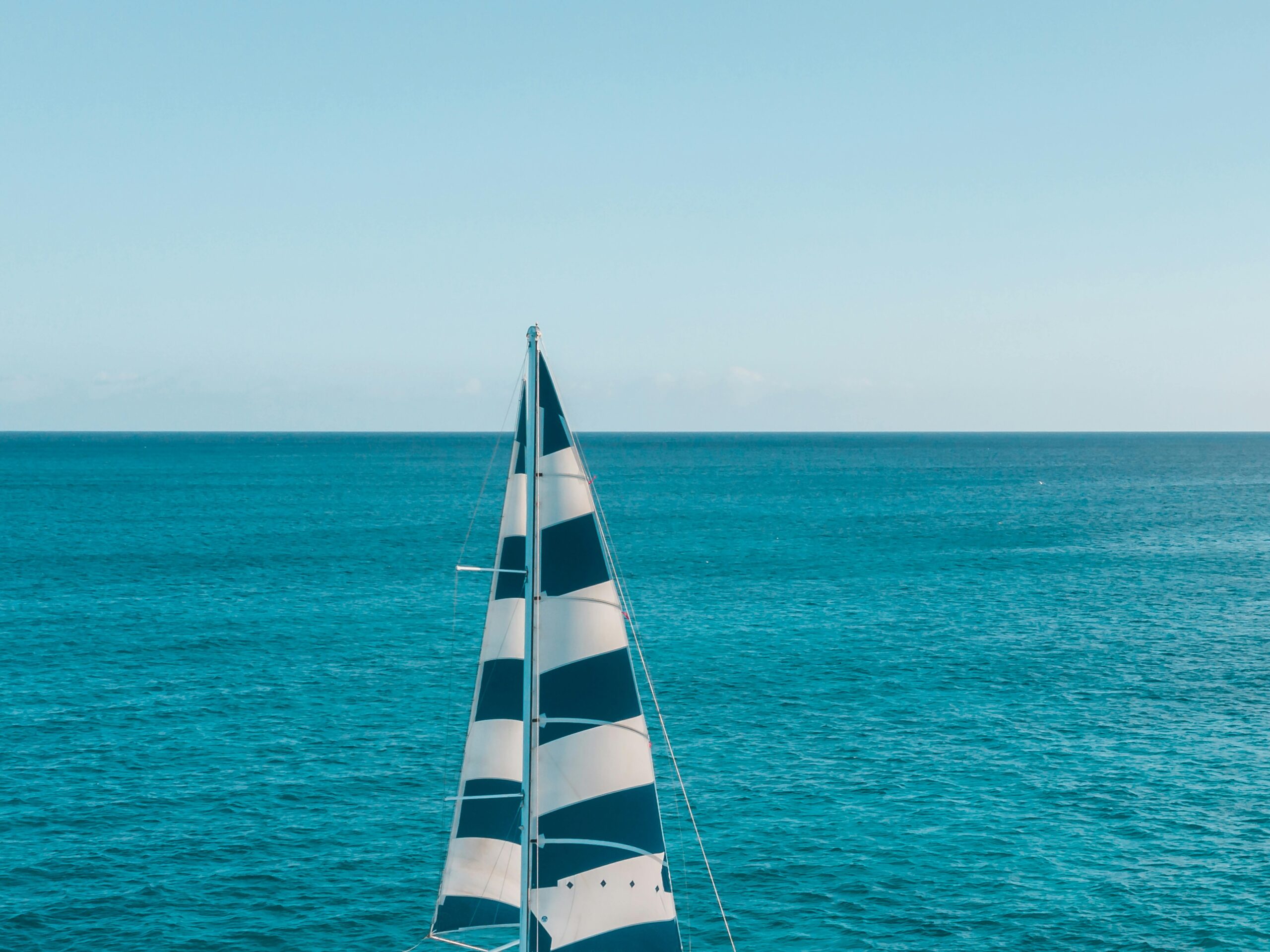 A sailboat with people cruising on a tranquil, open blue sea under a clear sky.